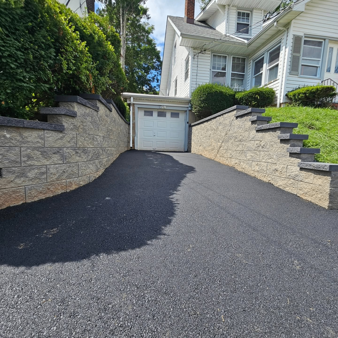 Finished retaining wall and fresh blacktop driveway at a residential property